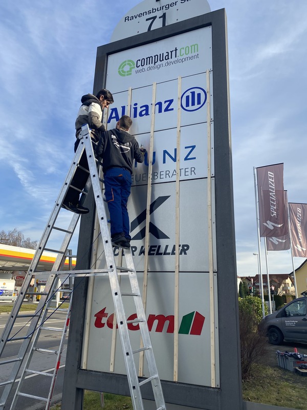 Mann montiert ein Schild mit Holzleisten.